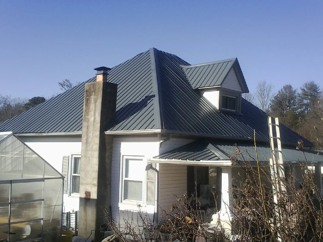 Dark blue standing seam metal roof on a white farmhouse with dormer — Slate & Tile Roof Repair by Roofing Brothers in Thompson