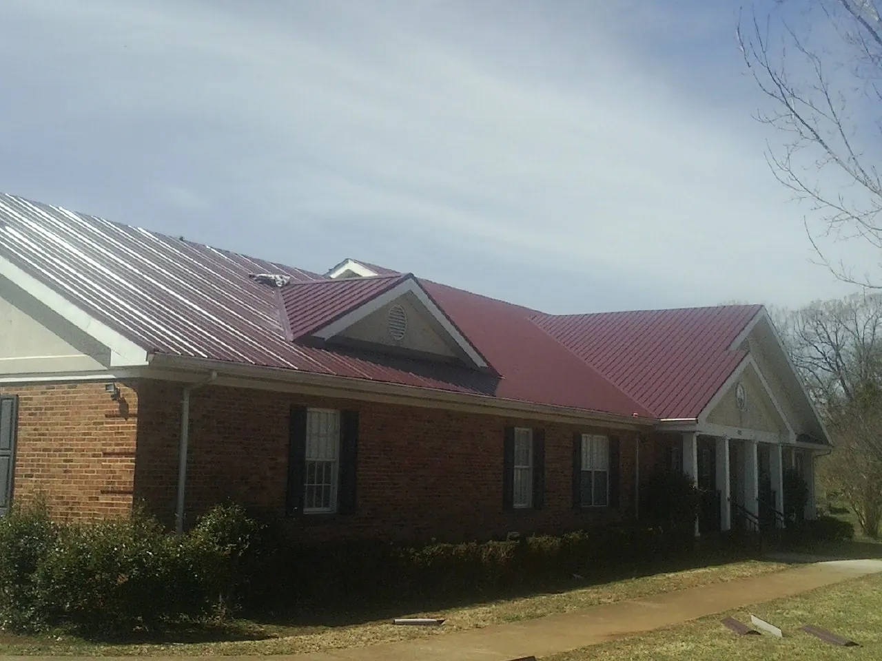 Red metal roof with gabled entries on a long brick building, from a Hail Damage Roof Repair job in Thompson